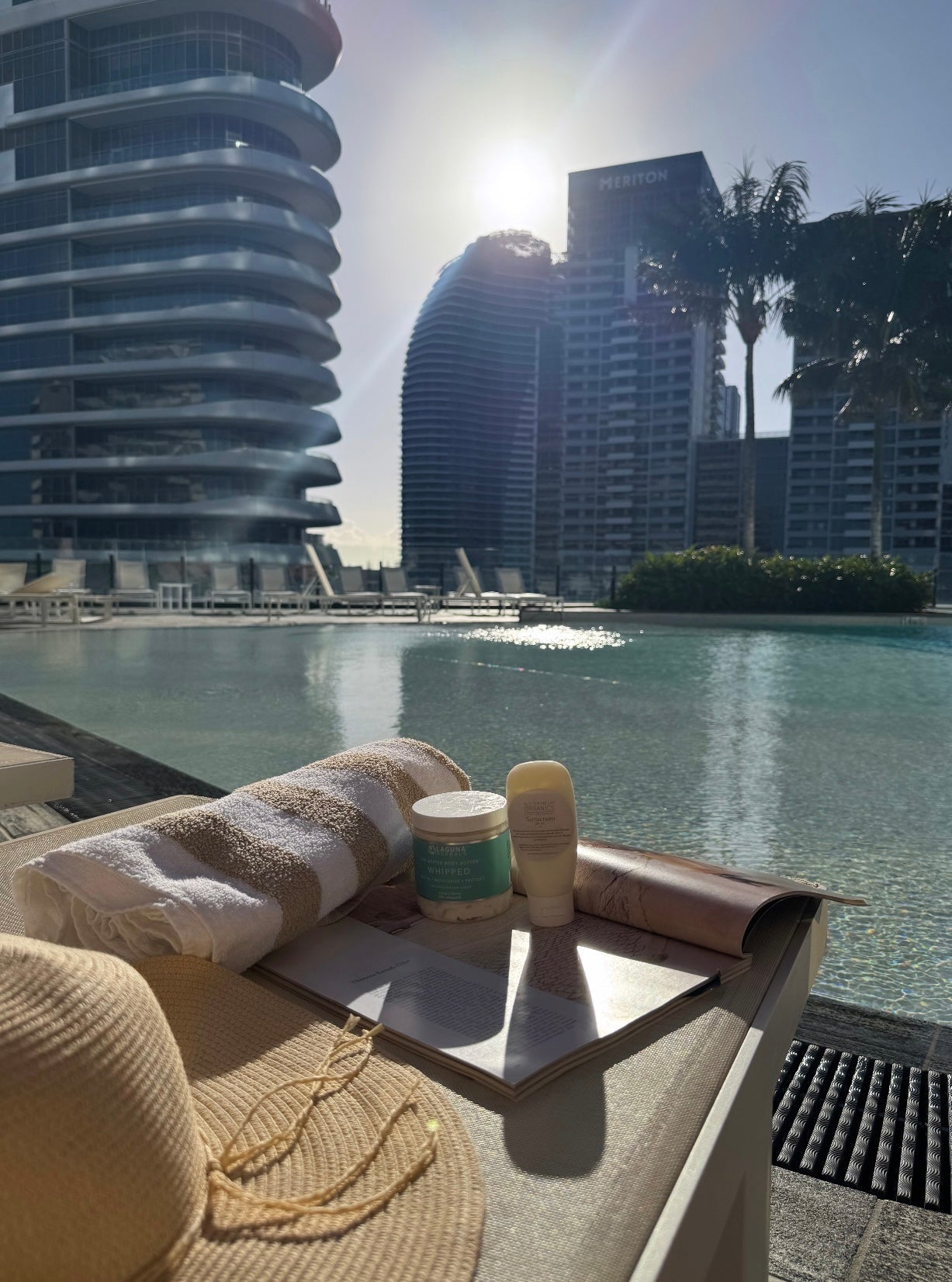 Sunscreen beach towel sun hat next to swimming pool summer aesthetic image