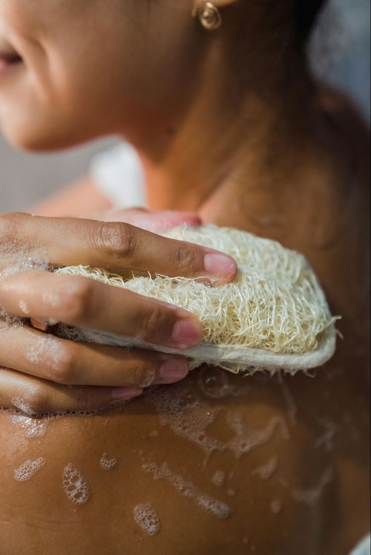 female hand holding eco friendly loofah in shower setting closeup showing her neck and hand