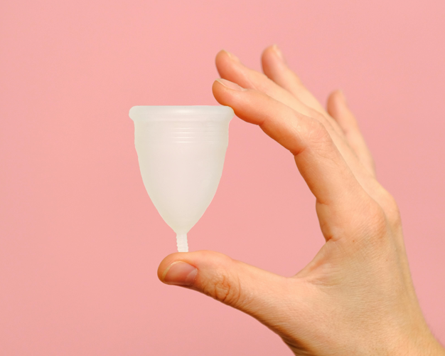 image of female hand holding a ecofriendly menstrual cup in a well lit bright orangey pinkish background
