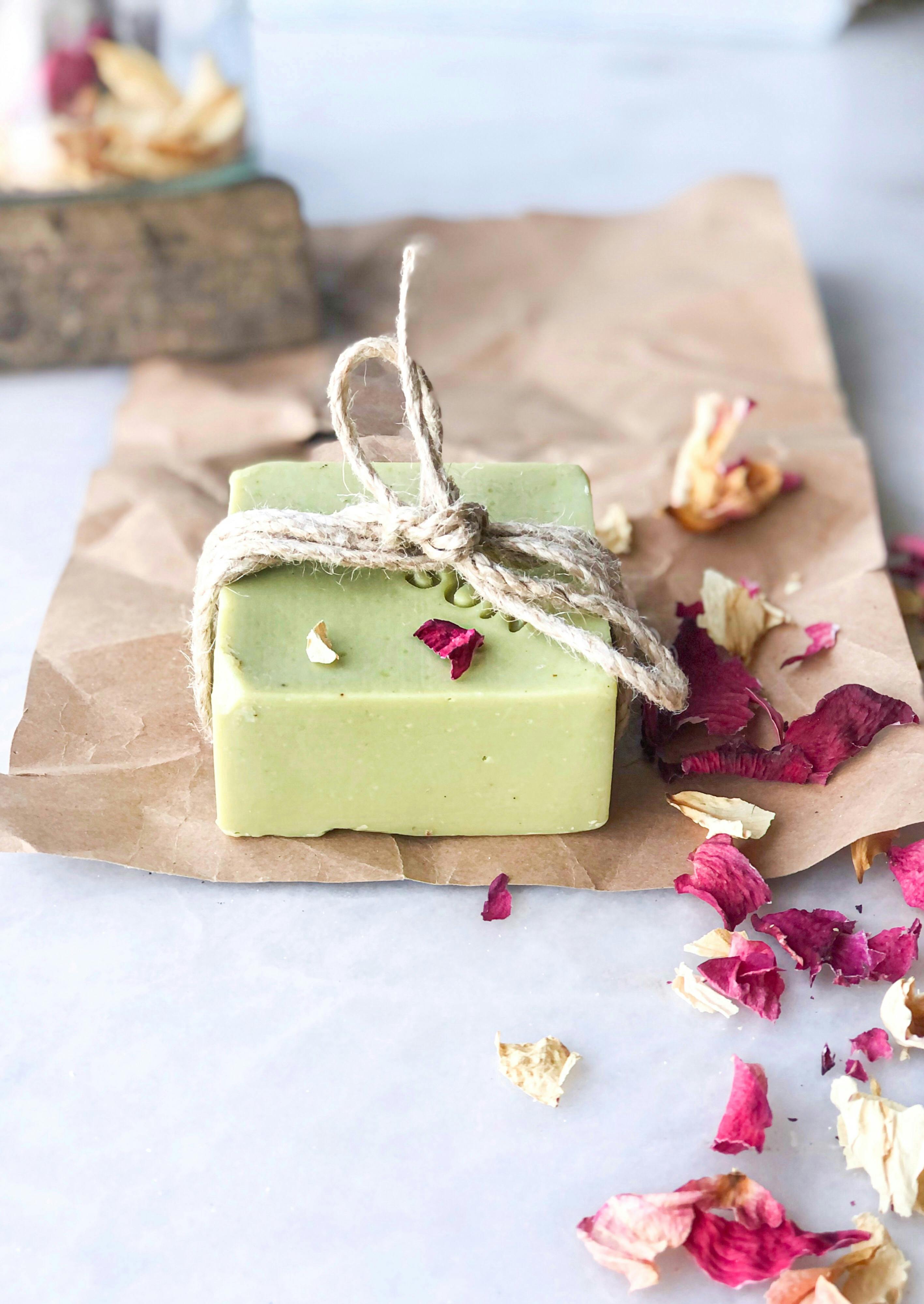 green zero waste shampoo bar on top of eco friendly packaging and rose petals 