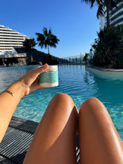 whipped body butter shot held by tanned model with her legs pointing at pool side aesthetic backdrop