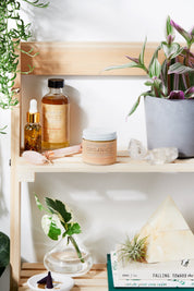 Organic Hydrating Facial Moisturizer with Aloe & Rosehip Oil closed/lidded product image in aesthetic shelf backdrop with rose quartz and green leaves, crystals and books zoomed out photo angle