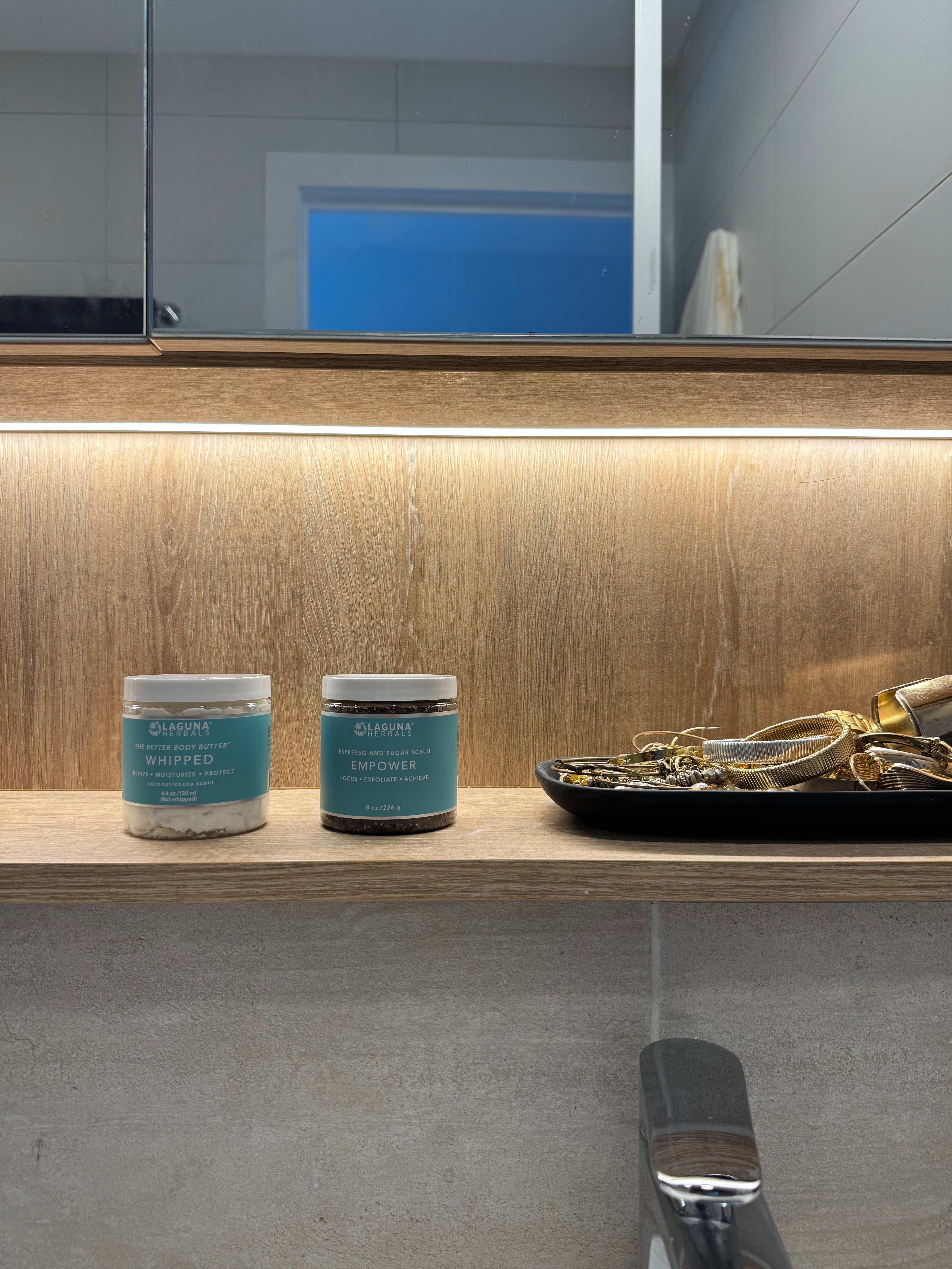 professional landscape shot of whipped body butter and coffee body scrub on an aesthetic wood shelf