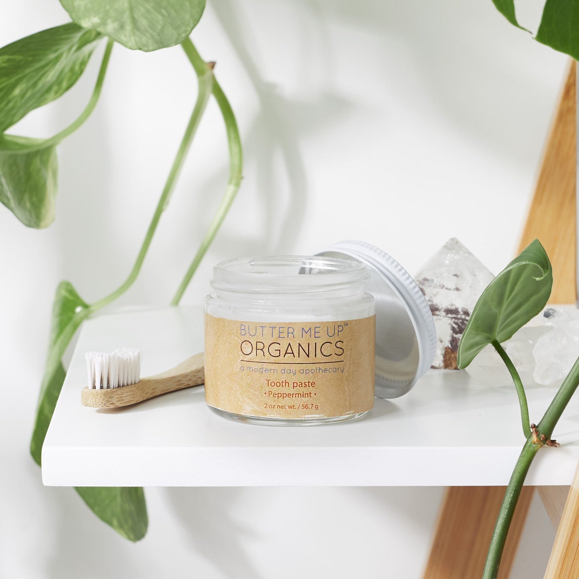 opened organic white toothpaste in glass jar with toothbrush and leaves in white backdrop