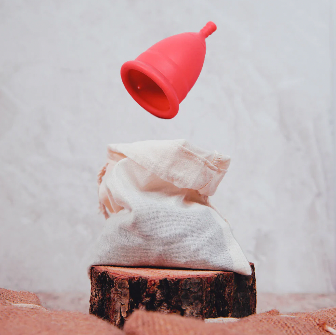 Pink Vegan & Silicone-Free Menstrual Cup in air with a beige bag underneath in aesthetic white and brown backdrop