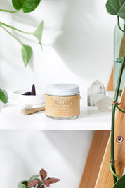 organic white toothpaste in glass jar with toothbrush, crystals and leaves in white backdrop