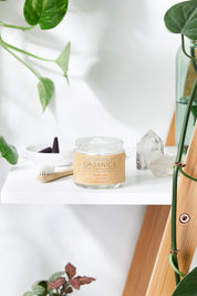 opened organic white toothpaste in glass jar with toothbrush, crystal and leaves in white backdrop
