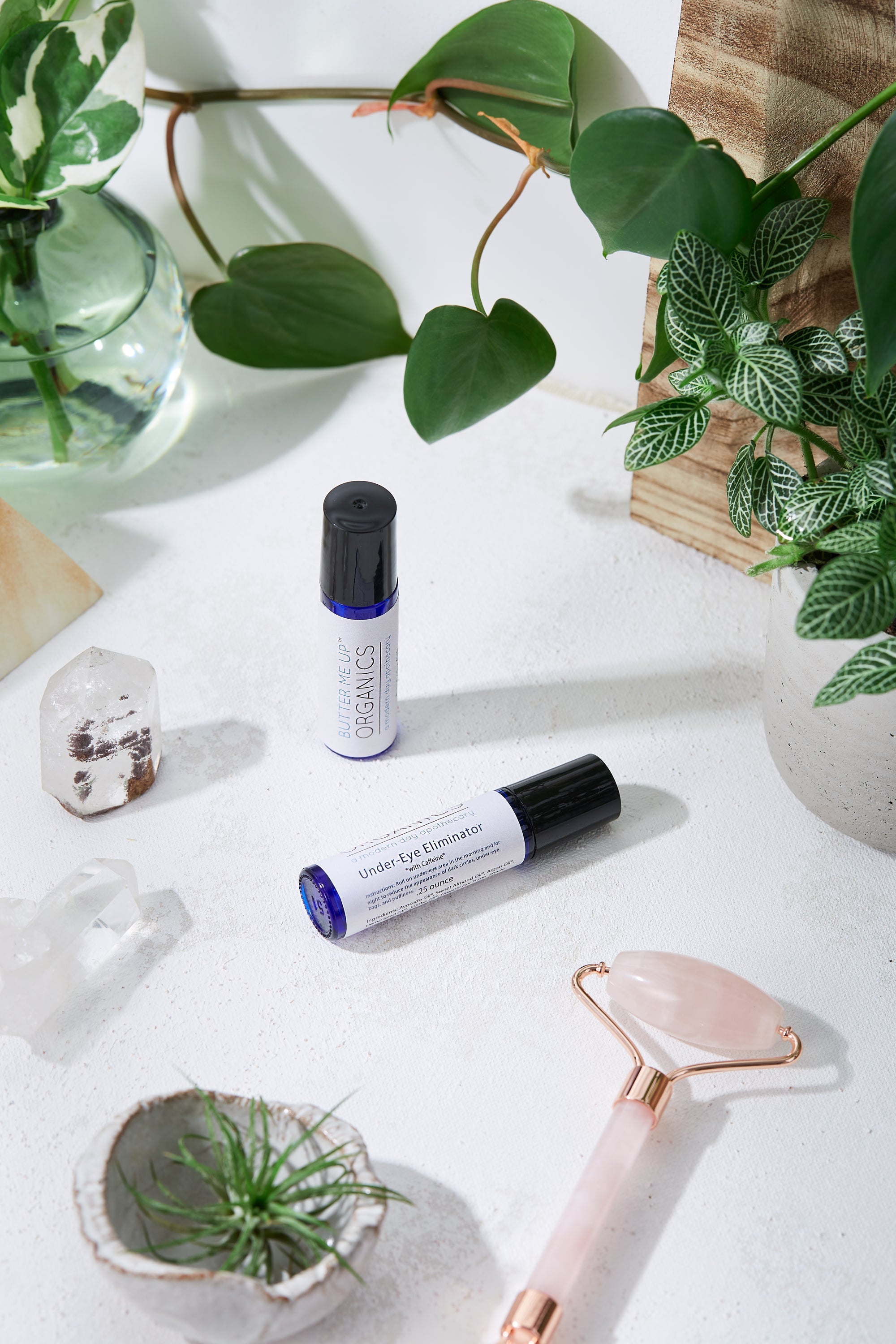 product image of Organic Caffeine Eye Repair Serum in 2x different size options in aesthetic white backdrop with green leaves and rose quartz