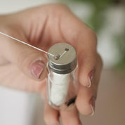 Biodegradable White Charcoal Dental Floss in glass bottle with a hand holding the bottle and pulling the floss