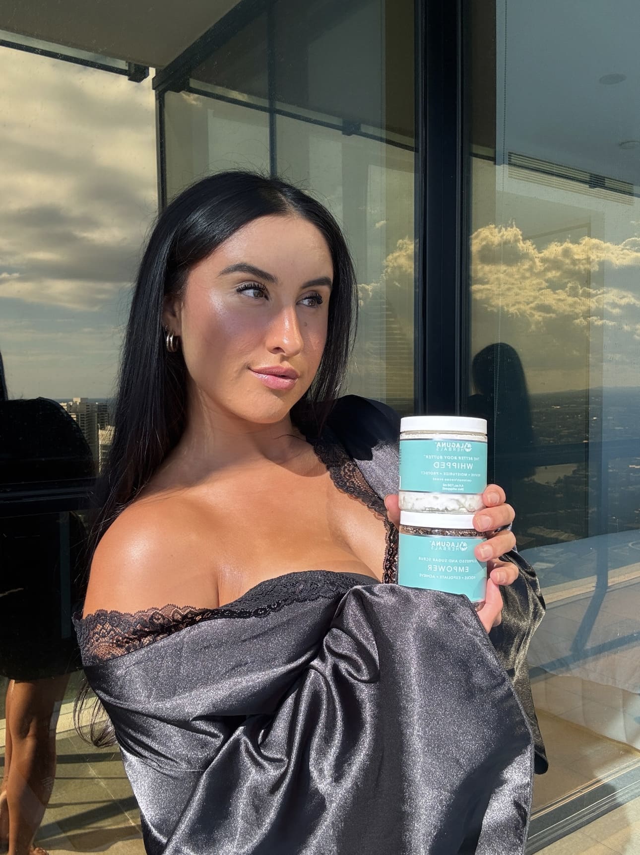 tanned model showcasing whipped body butter and coffee scrub products in aesthetic backdrop