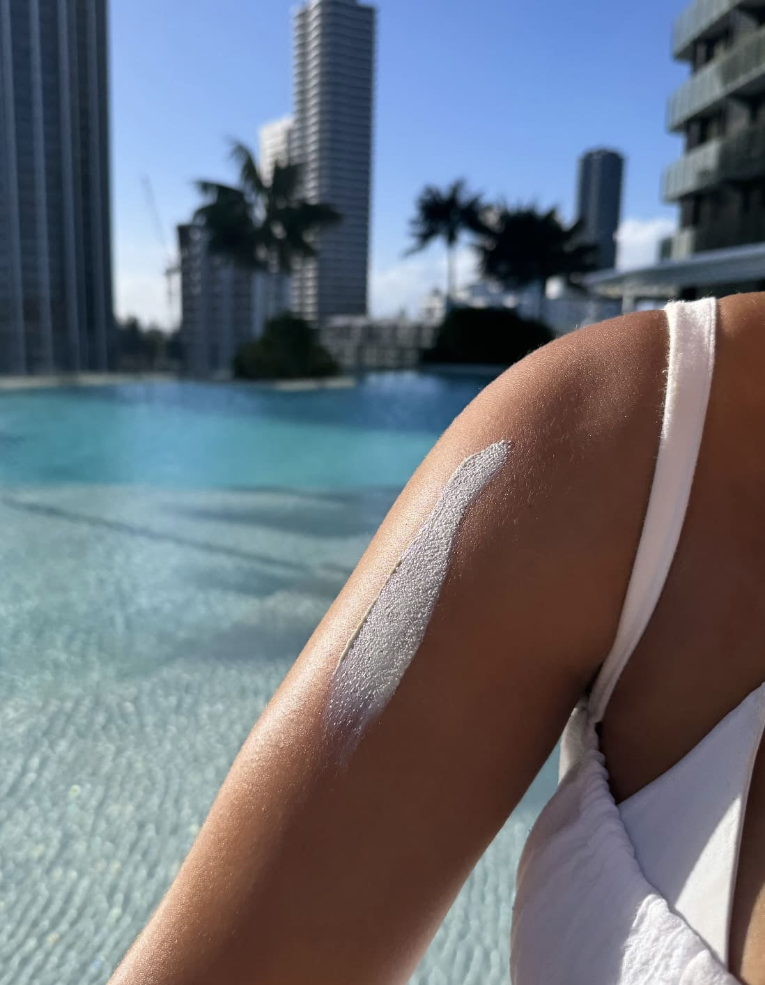 close up shot of organic non white cast sunscreen on tanned arm with aesthetic beach pool background summer