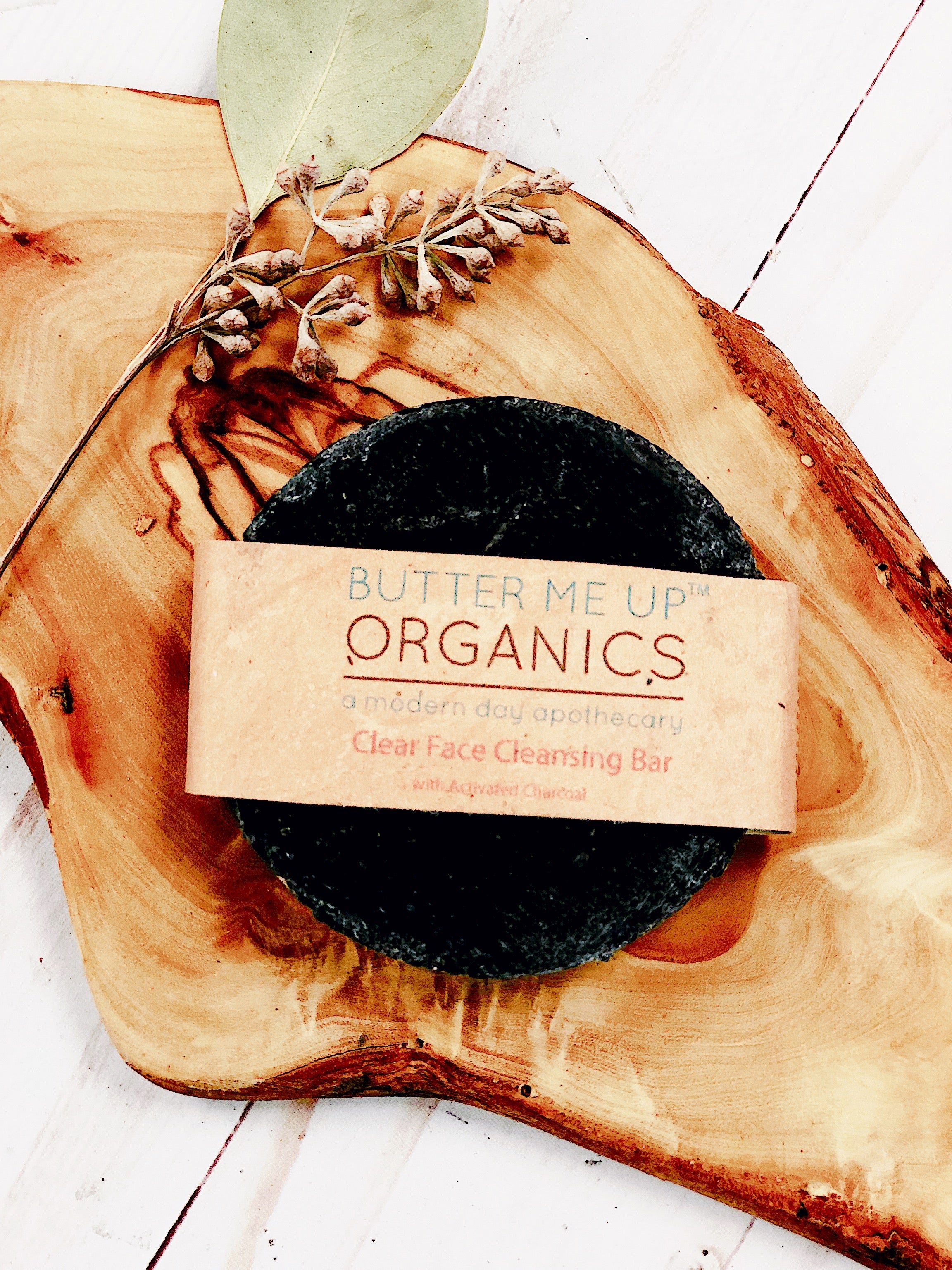 Organic Charcoal Purifying Face Soap Bar product image close up in brown aesthetic packaging but also showing the face bar in an aesthetic wooden bark backdrop with sage green leaves