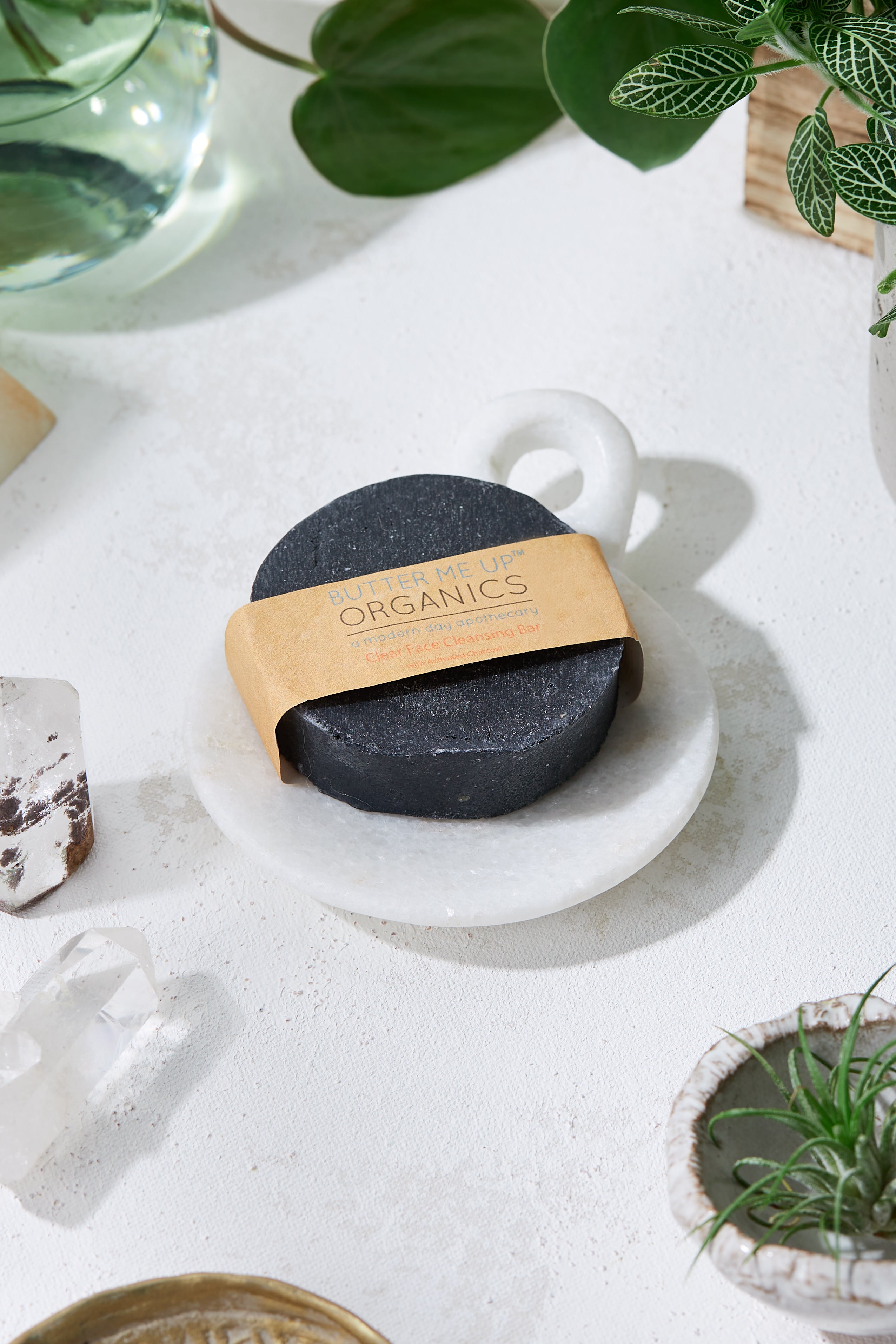 Organic Charcoal Purifying Face Soap Bar product image close up in brown aesthetic packaging but also showing the face bar in an aesthetic white marble backdrop with crystals and leaves