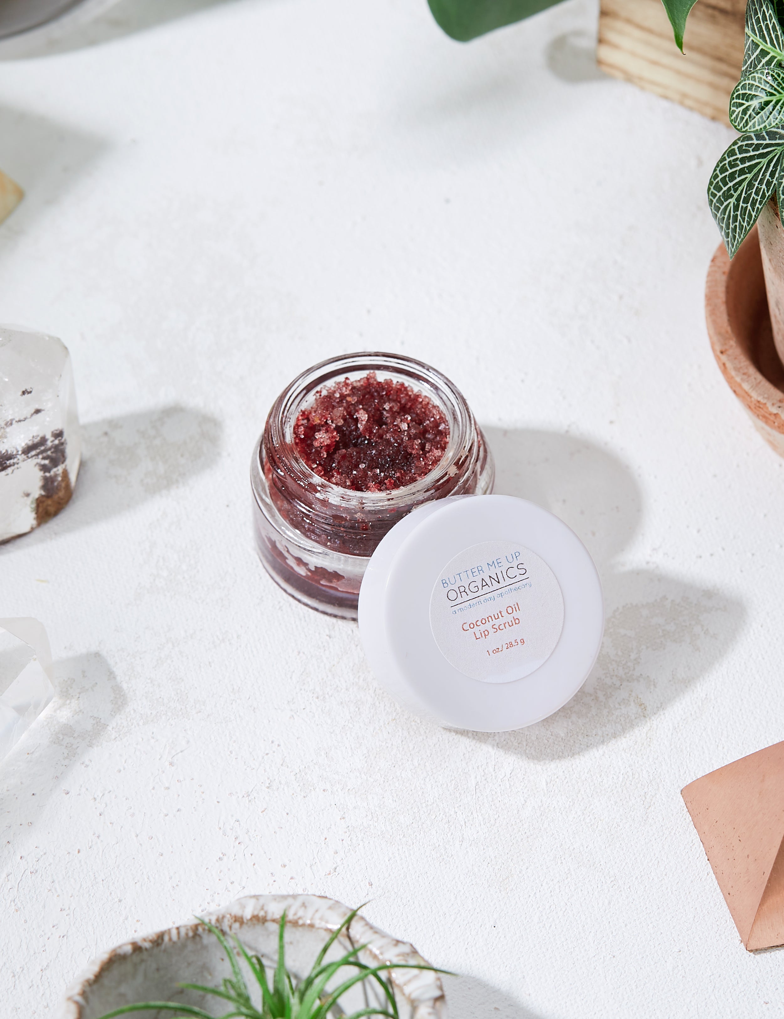 product image of opened Organic Coconut Lip Scrub in white marble aesthetic backdrop and green leaves