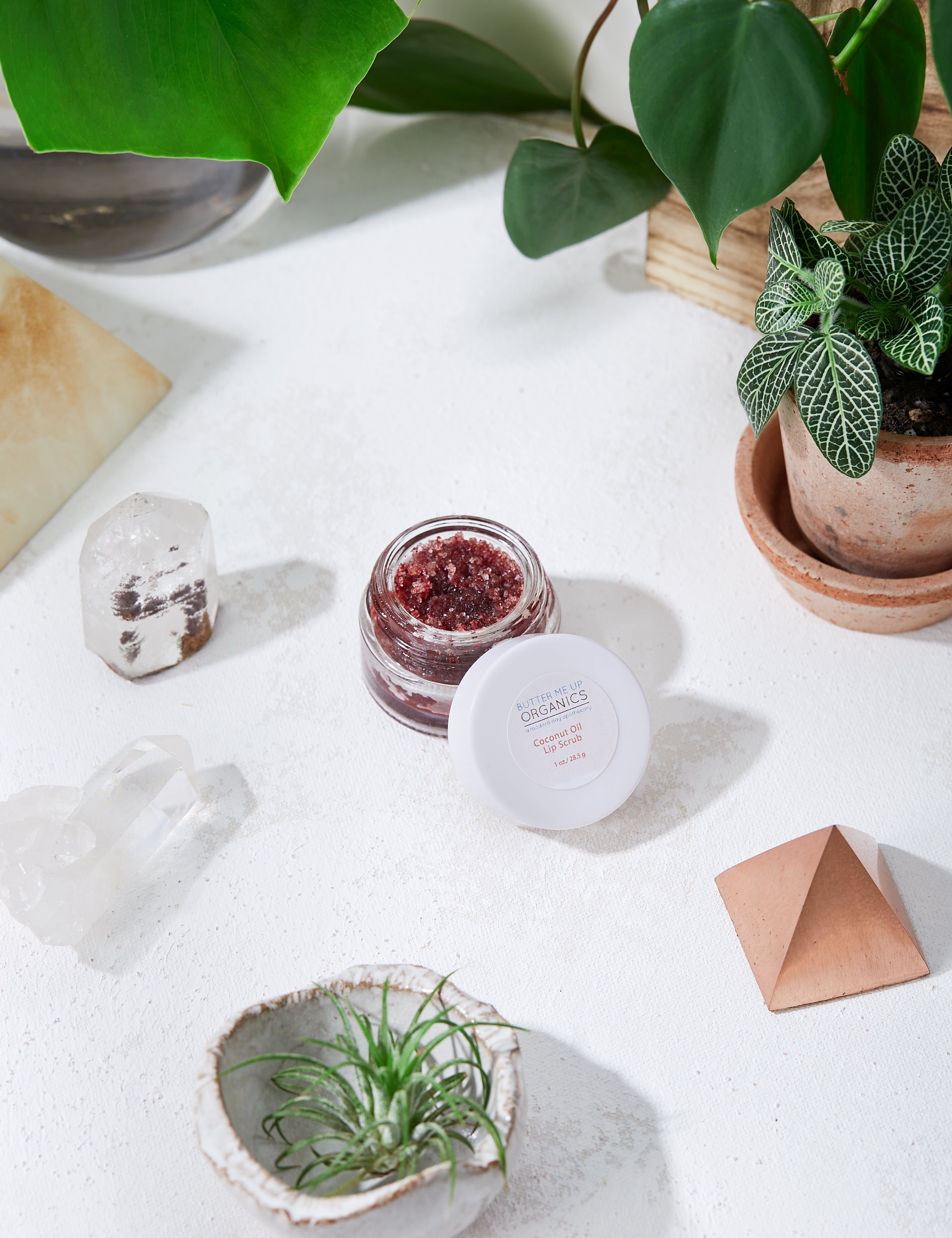 opened Organic Coconut Lip Scrub product image birds eye view in white marble aesthetic backdrop with crystals and green leaves