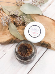 opened product image of the organic Chocolate Lip Scrub with aesthetic bark backdrop with sage green leaves