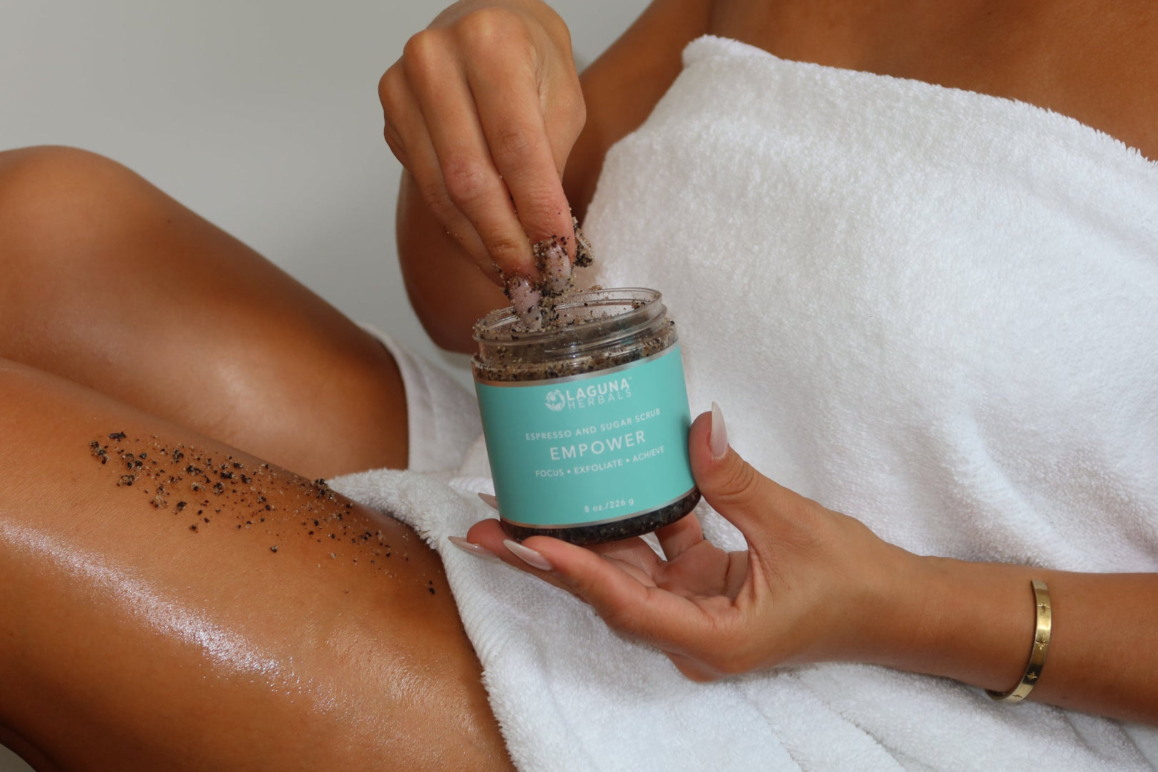 Person applying a exfoliating scrub to their leg with a jar labeled 'Skeptic'.
