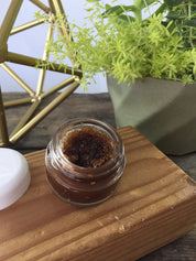 opened product image of the organic Chocolate Lip Scrub with aesthetic bark backdrop with sage green leaves close up