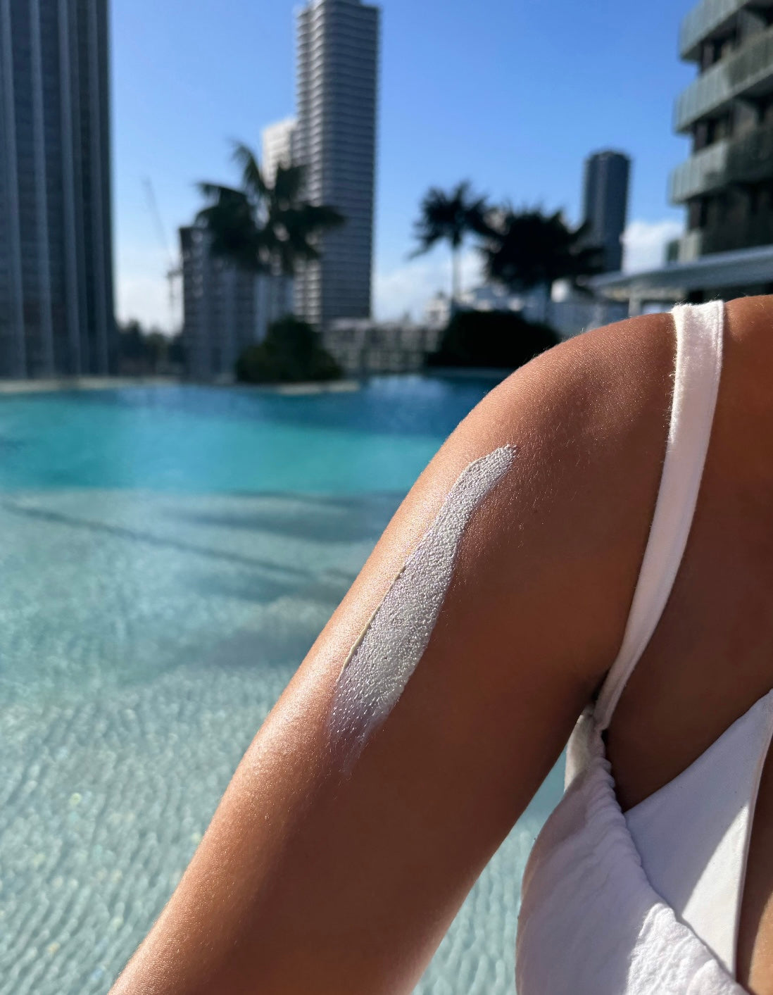 close up image of organic sunscreen applied on tanned arm in a poolside beach backdrop