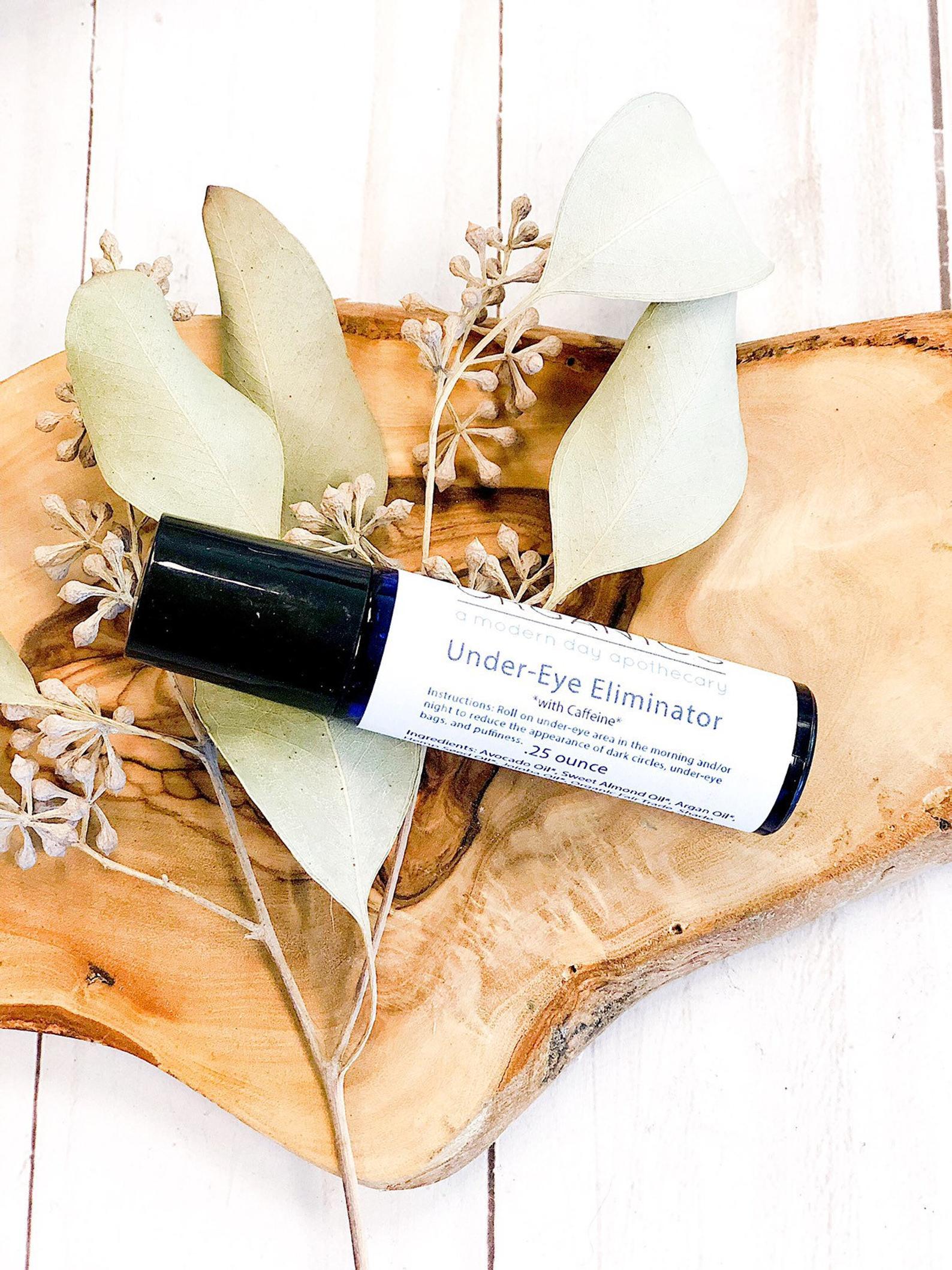 product image birds eye view of Organic Caffeine Eye Repair Serum in aesthetic wooden bark backdrop and sage green leaves